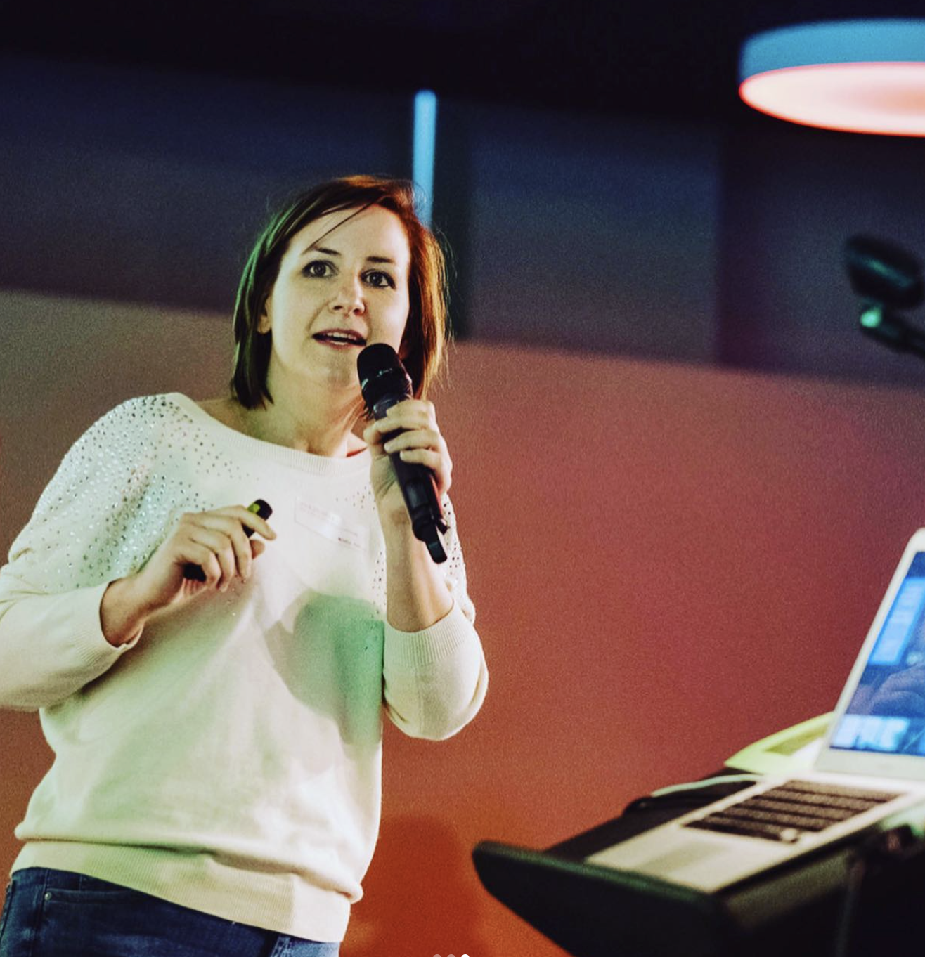 Een vrouw die spreekt op een donker podium, verlicht in kobaltblauw