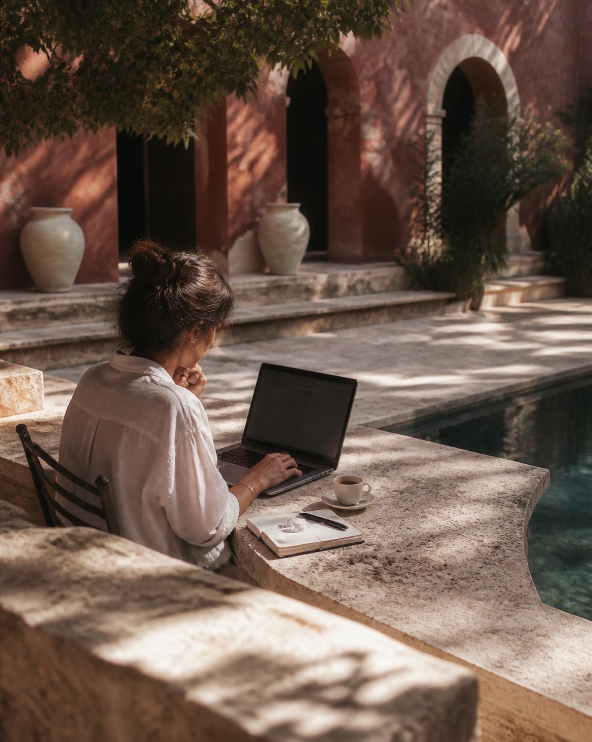 Iemand werkt alleen op een laptop op een terras naast een zwembad
